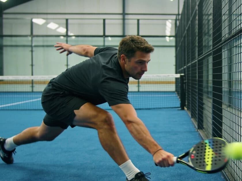 A padel player lunging low to reach a ball at the net